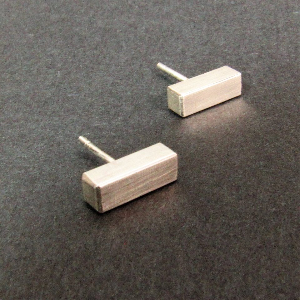 A pair of silver bar stud earrings. The earrings are rectangular in shape and have a brushed finish.