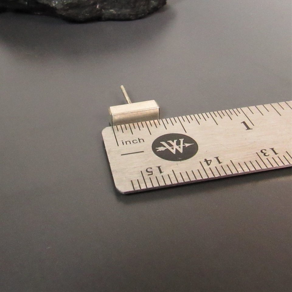 A sterling silver bar earring measuring approximately 1/2 inch in length. The earring is shown next to a ruler for size reference.