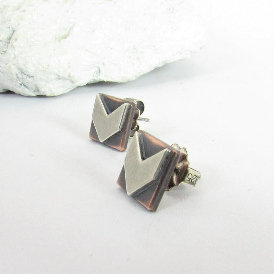 Side view of a pair of silver and copper earrings with a geometric arrow design. The earrings are square shaped with a silver arrow pointing down in the center of each earring. SS clutch backs included.