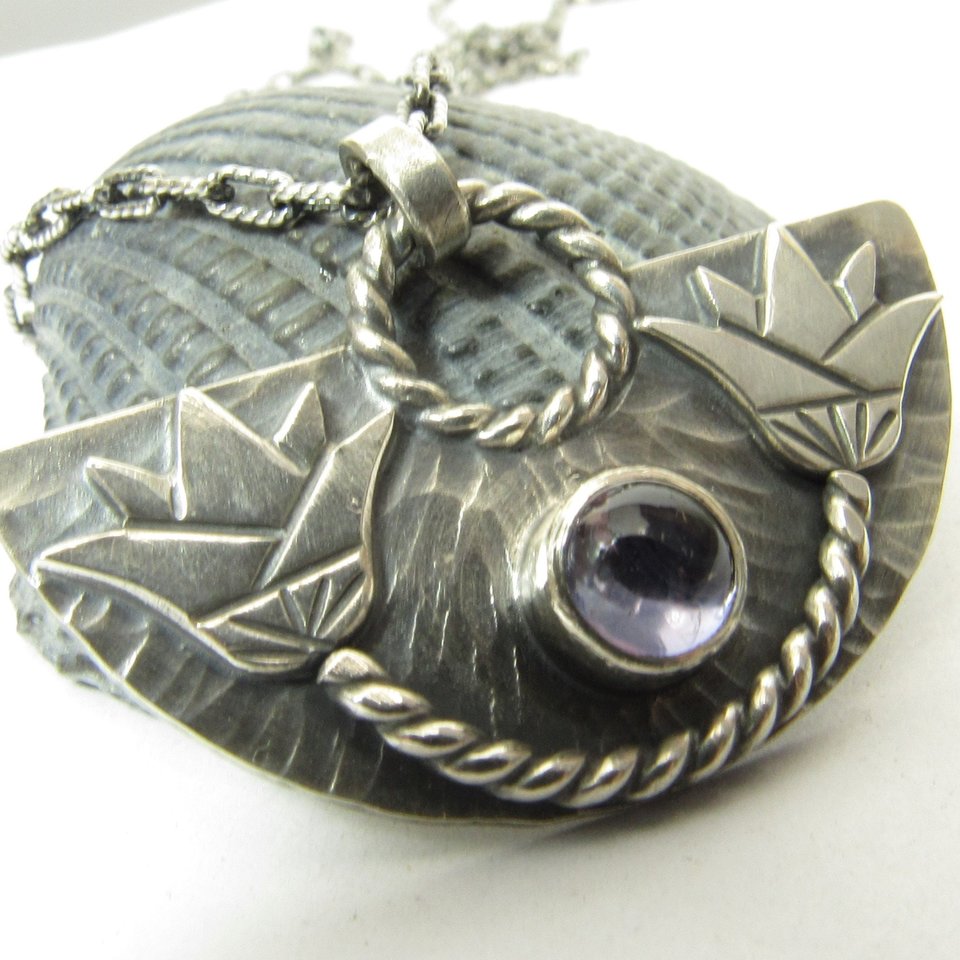 A striking and unusual lotus pendant necklace with an Egyptian theme and a lovely bezel set violet iolite. Pendant measures 7/8 inch tall and 1 and 3/8 inch wide. Fan shape with double lotus design. 18 inch SS chain and handmade findings.