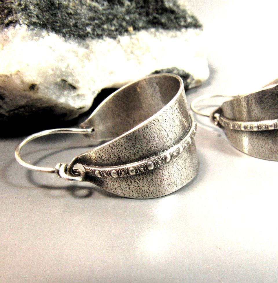 Classic basket style argentium silver hoops with a decorative strip of beaded wire against a sand textured back ground. Oxidized and polished, finished with securely wrapped sterling ear wires. Background is black and white rock on grey paper 1.25 inch tall,  7/8 inch wide.