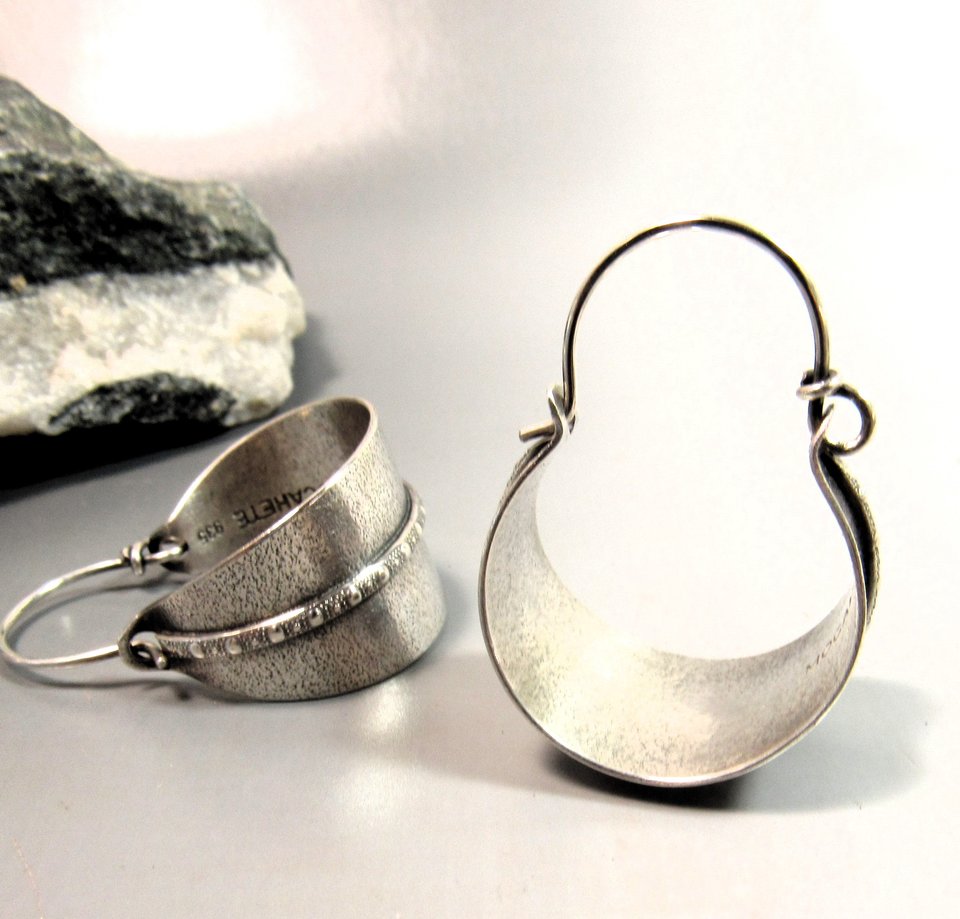 Sterling silver hoop earrings basket style fancied up with a strip of patterned  silver wire against textured argentium silver. A perfect sterling silver hoop earring for every occasion!  Oxidized, polished, finished with sterling ear wires. 1.25" or 3.1cm tall,  7/8" or 2.22cm wide. Displayed on neutral background with black and white rock.