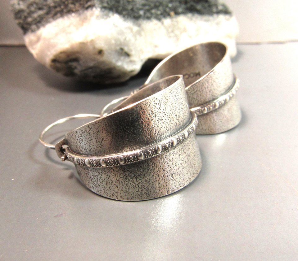 Side view of Sterling silver hoop earrings basket style fancied up with a strip of patterned  silver wire against textured argentium silver. A perfect sterling silver hoop earring for every occasion!  Oxidized, polished, finished with sterling ear wires. 1.25" or 3.1cm tall,  7/8" or 2.22cm wide. Displayed on neutral background with black and white rock.
