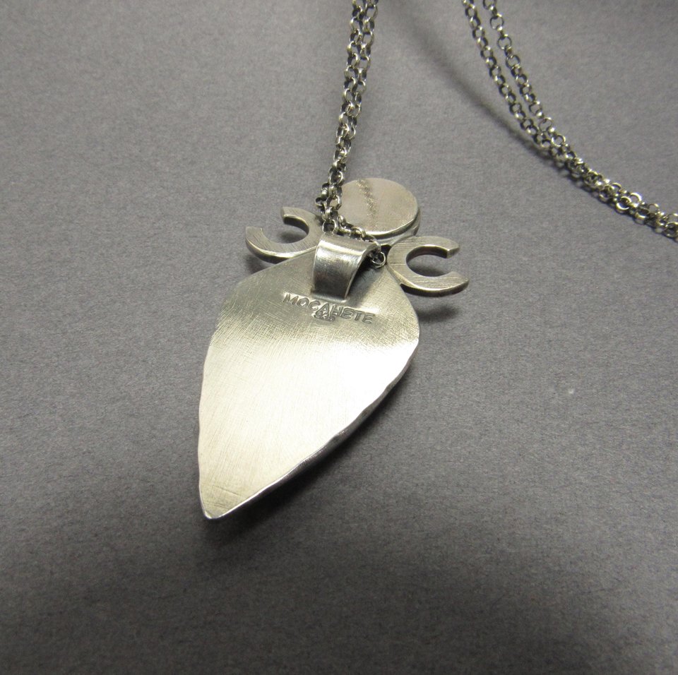 Reverse side of Triple goddess / moon pendant necklace with a faceted citrine and large lapis lazuli cabochon crafted from argentium sterling silver, fine silver. Pendant measures 2 inches from the top and is 7/8 inch across widest part and is suspended on a 18 inch sterling silver chain. Showing makers mark and purity. Displayed against grey background.