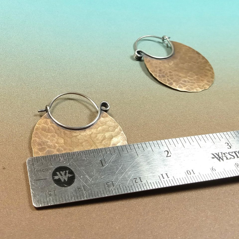 large bronze and silver hoop earrings against ruler to show width, blue and brown background.