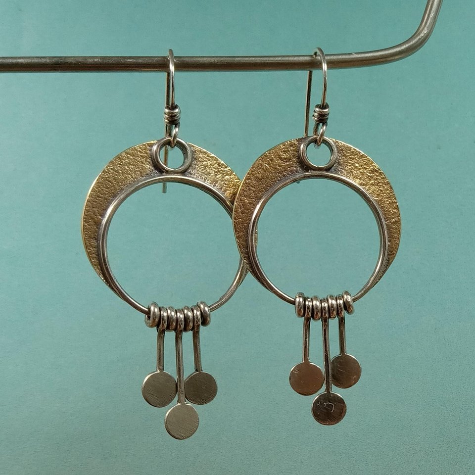 Mixed metal bronze and argentium silver crescent moon earrings on display stand on blue background.