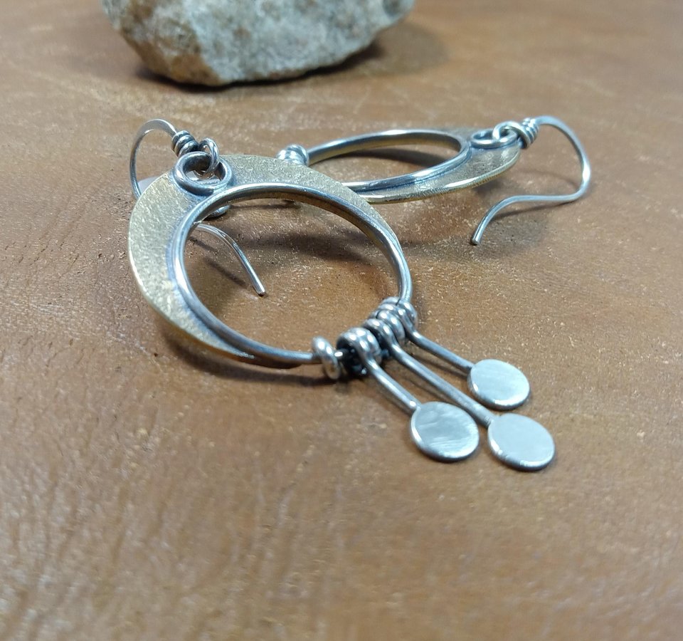 Side view of crescent moon dangle earrings with paddle fringe by Mocahete. Brown background.