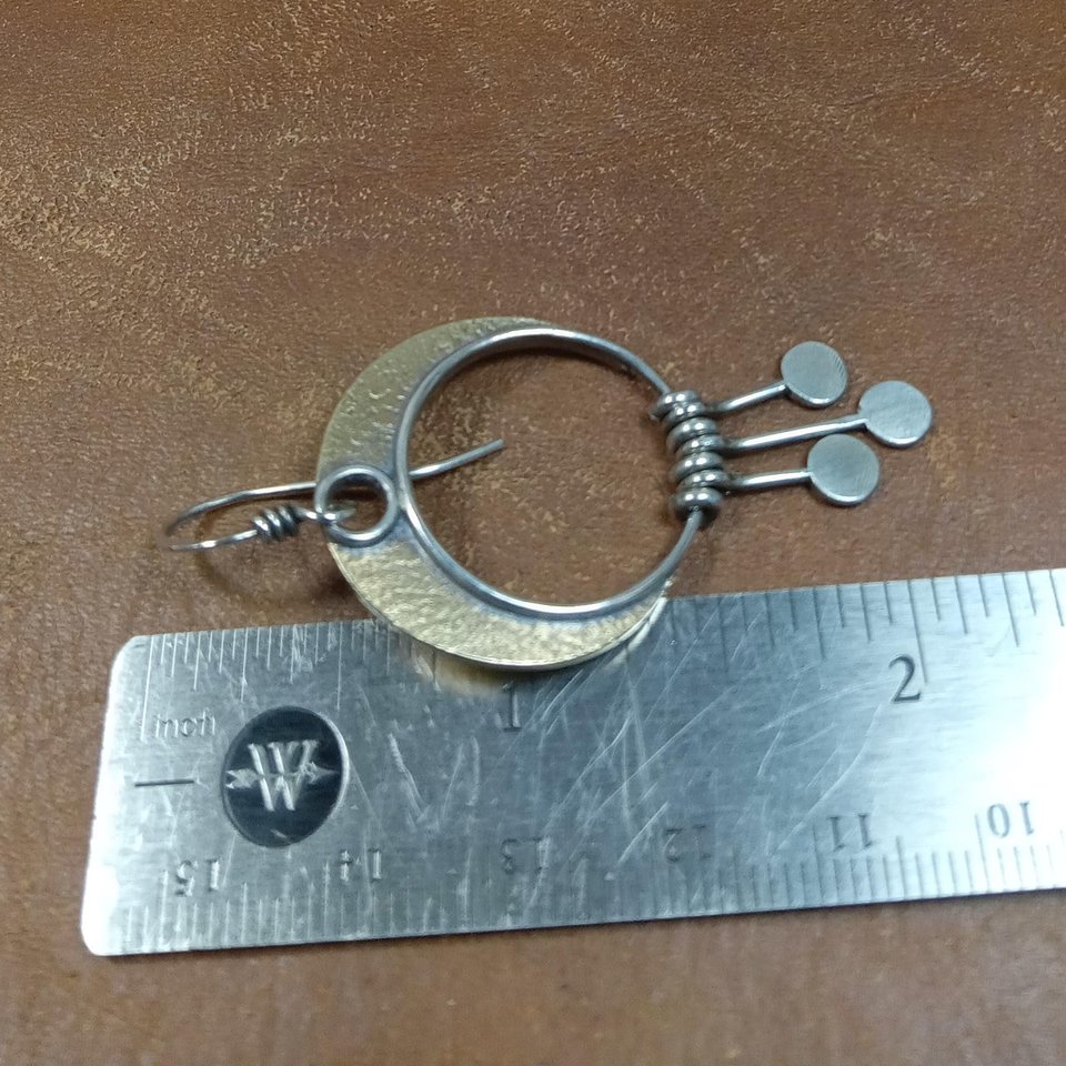 Bronze and Argentium silver crescent moon dangle earrings against ruler on brown background.
