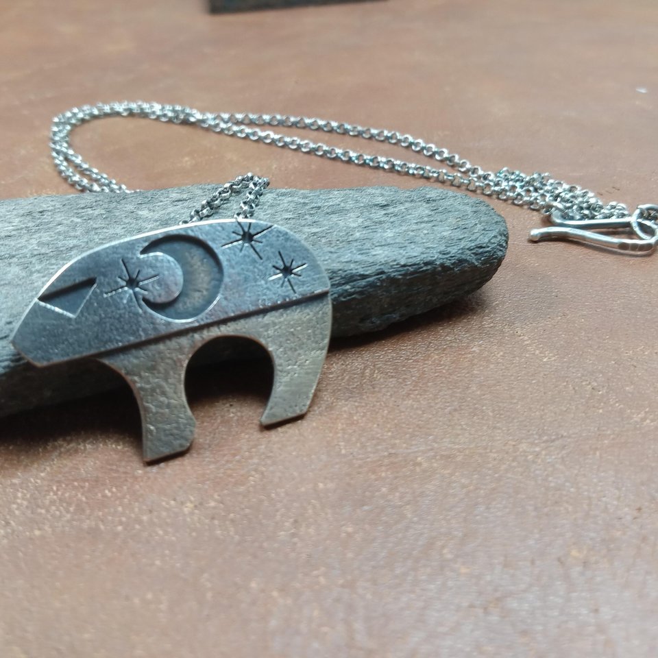 Bronze and silver bear necklace, Ursa major against rock on brown background.
