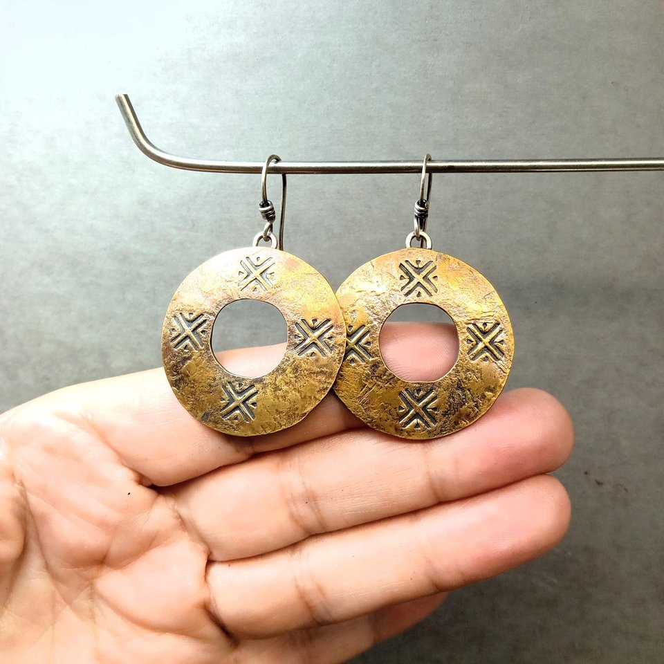 Mixed metal, bronze and silver coin style earrings hanging from stand against fingers to show detail