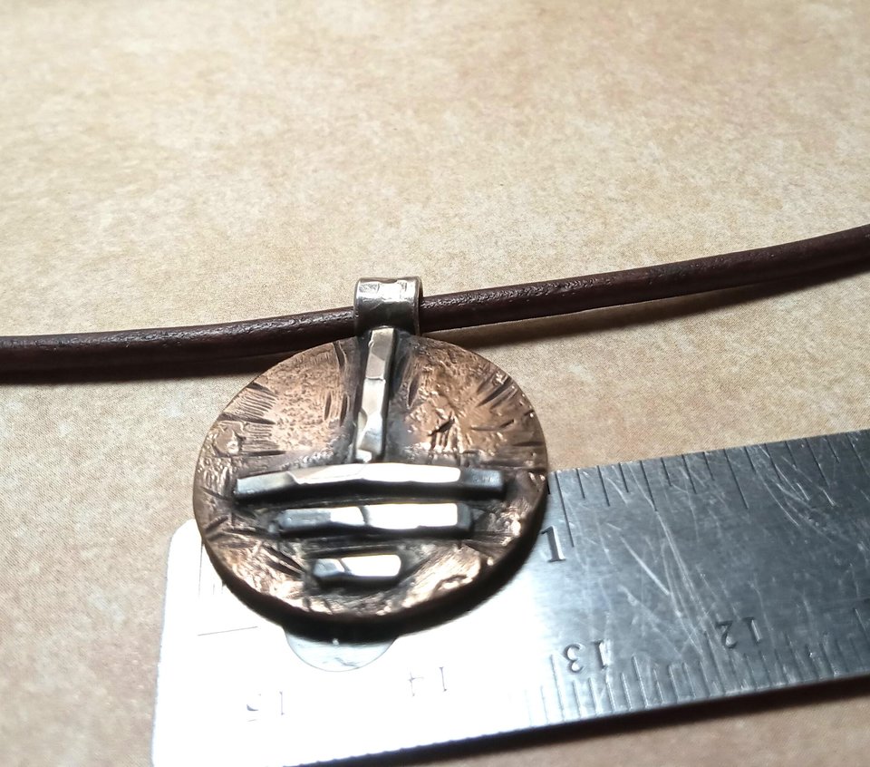 Grounding symbol pendant against ruler to show size.