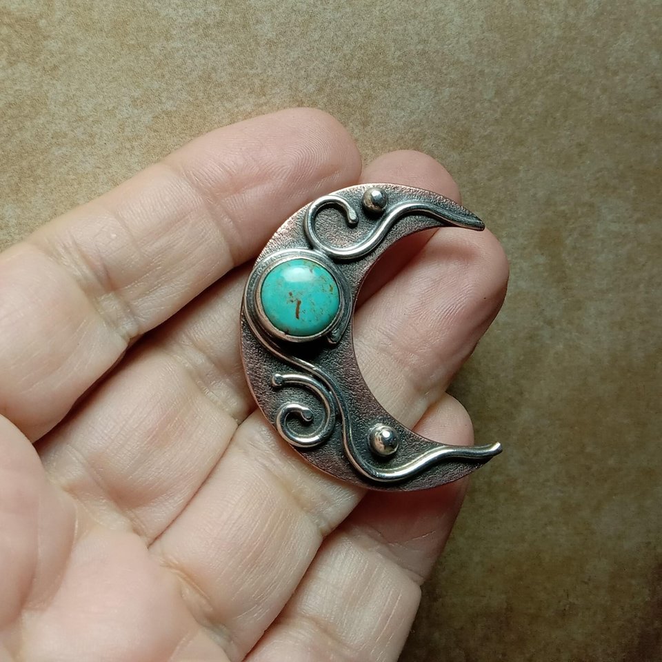 Copper, silver and turquoise moon pendant in hand.