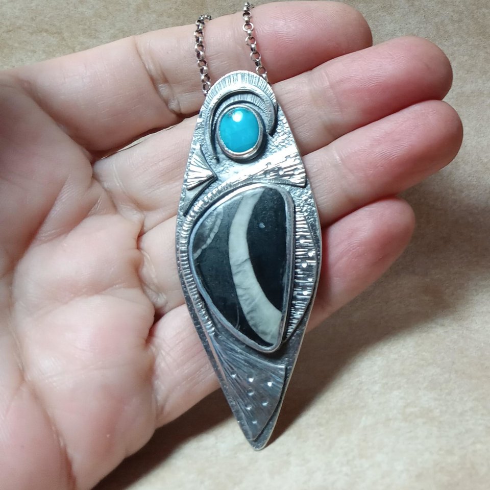 photo in hand of unique marine fossil and turquoise pendant crafted in argentium sterling silver