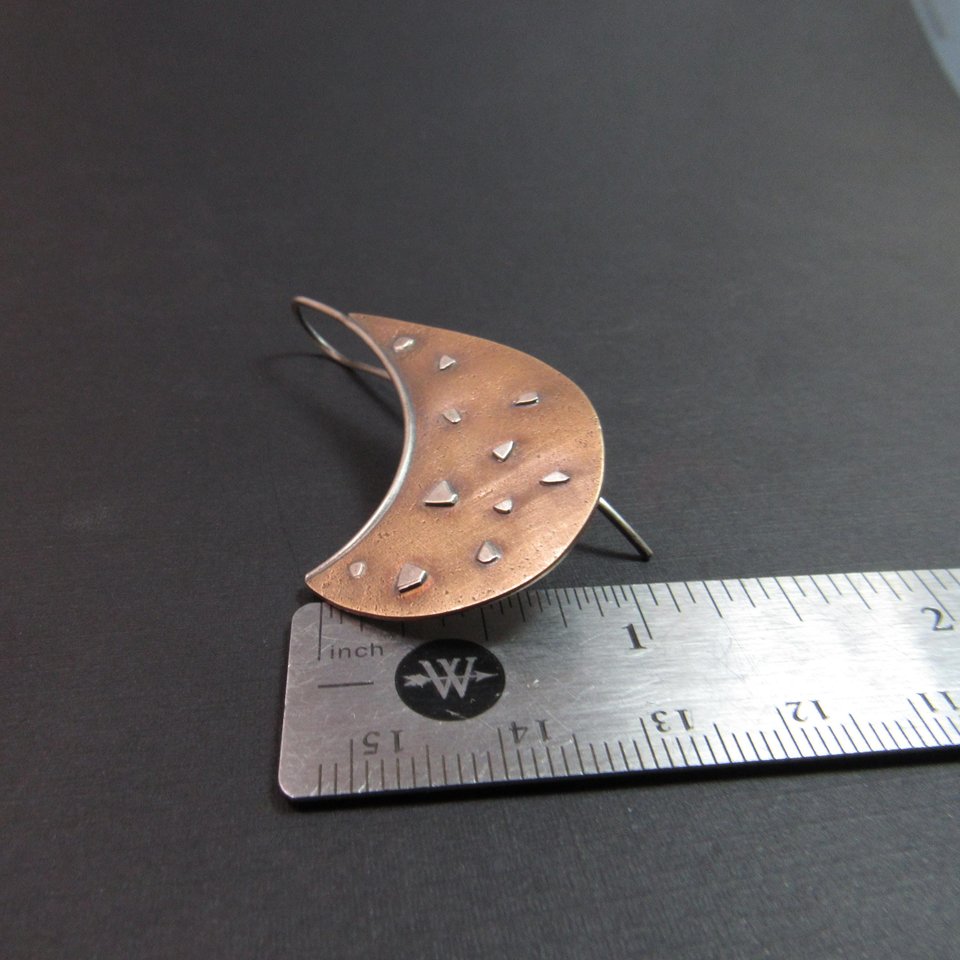 Avant garde style bronze and sterling silver earrings by Mocahete against ruler and black background.