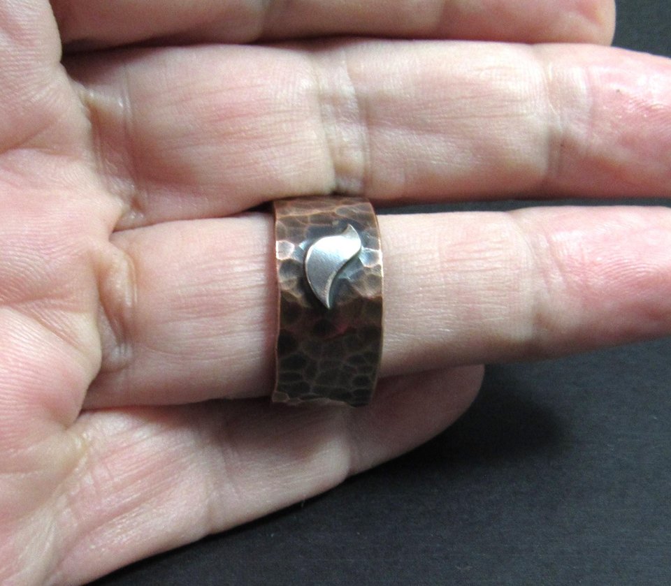 Bird ring on finger, hammered copper with silver bird on dark background.