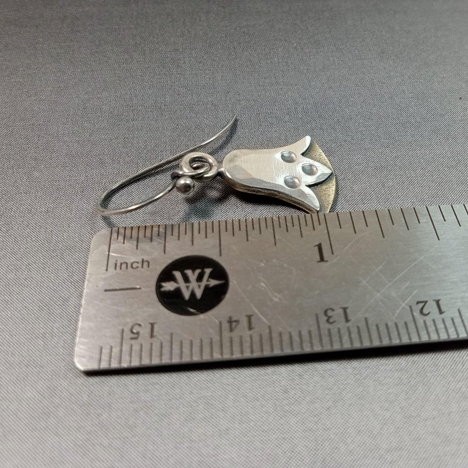 Mixed metal lotus earrings against ruler on grey background
