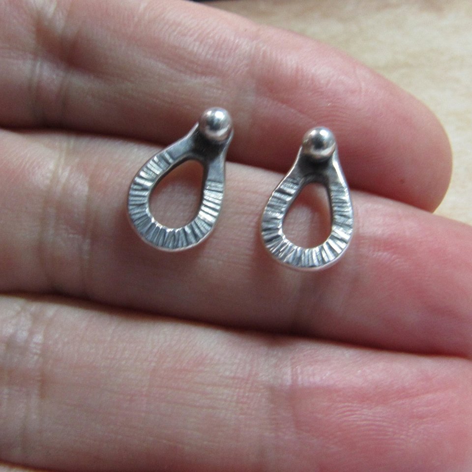 Sterling silver post back or stud earrings shaped like a raindrop and textured. A small orb of silver at the top is the crowning touch. Earrings measure 1/2" long and 1/4" wide. Comes with SS backs not pictured here.Displayed on in hand on light background.