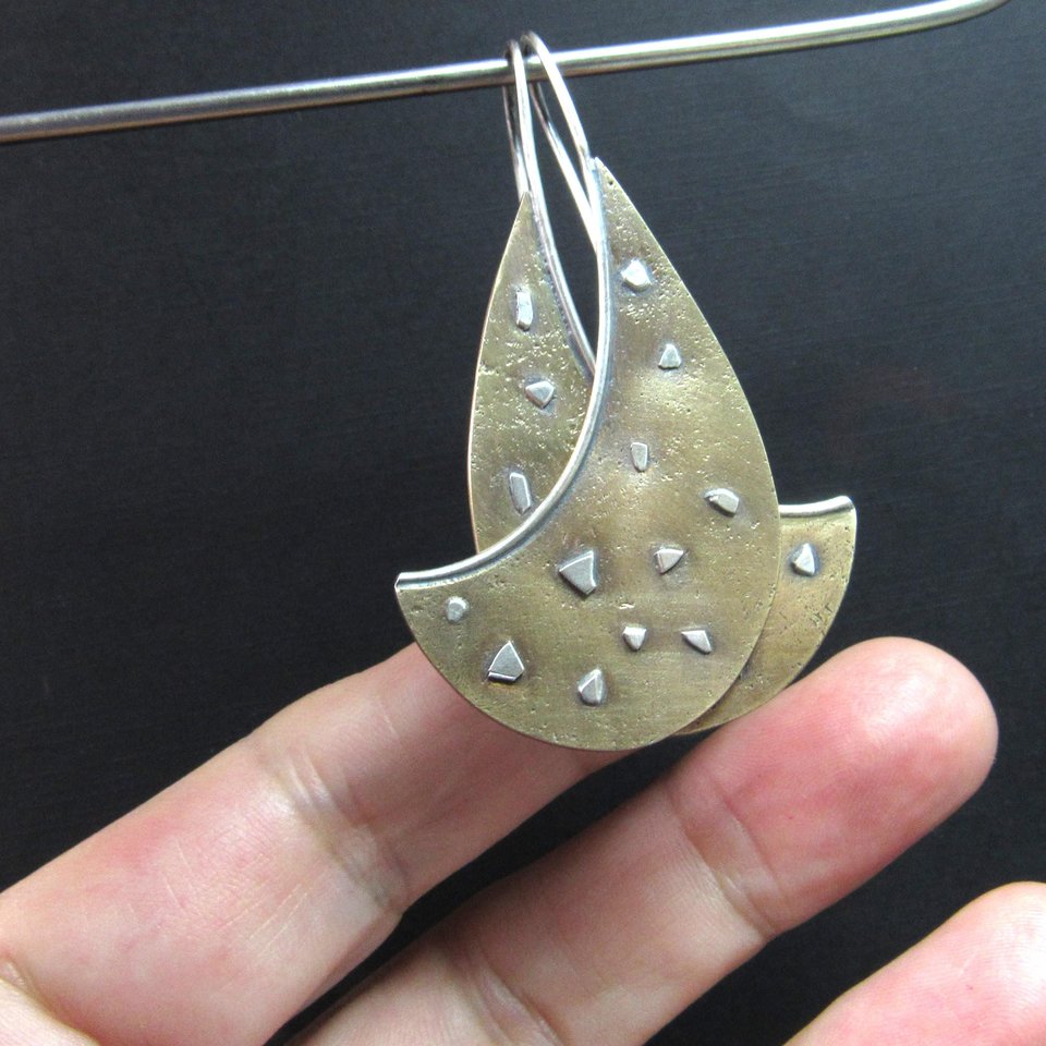 Mixed metal, bronze and sterling silver earrings with an avant garde spirit, photo against fingers on dark background.