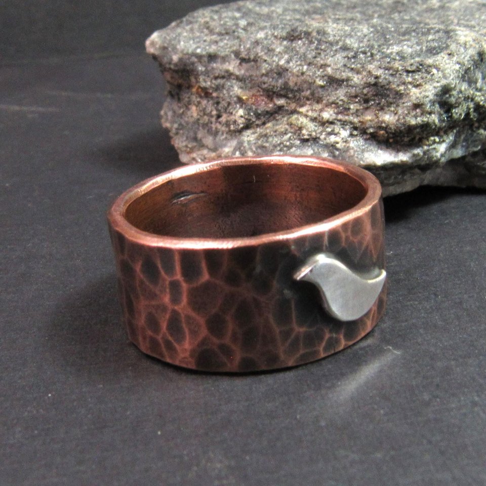 Rustic copper ring with silver bird, wide band perfect for men, women, unisex. Photo against rock on dark background.