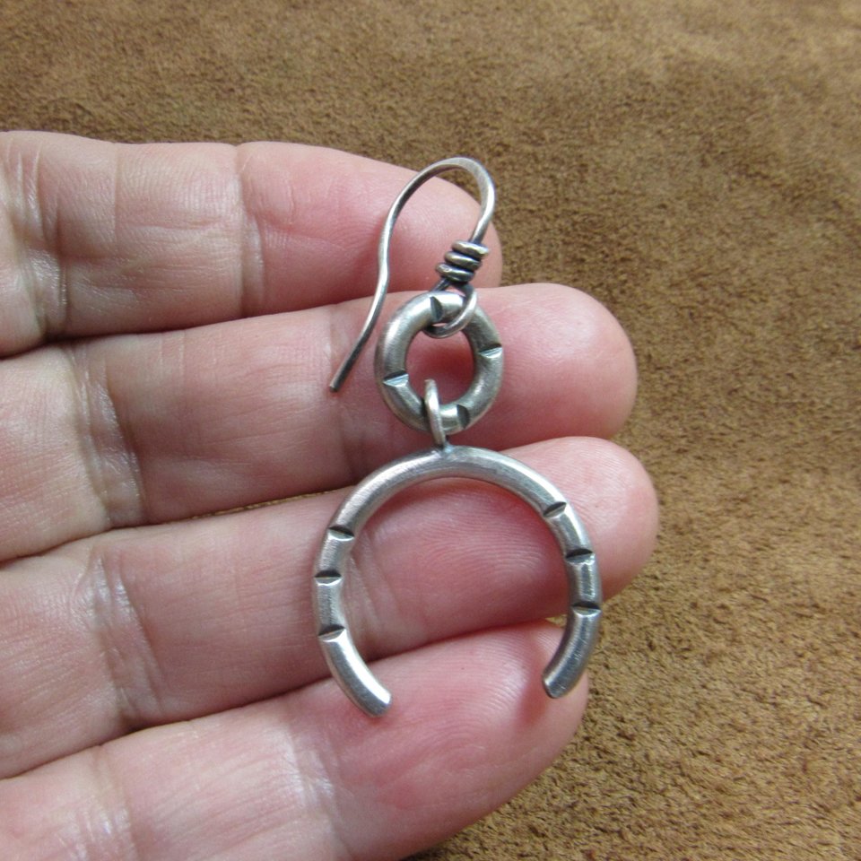 One of a pair of argentium open hoop earrings. Displayed in hand on brown leather.