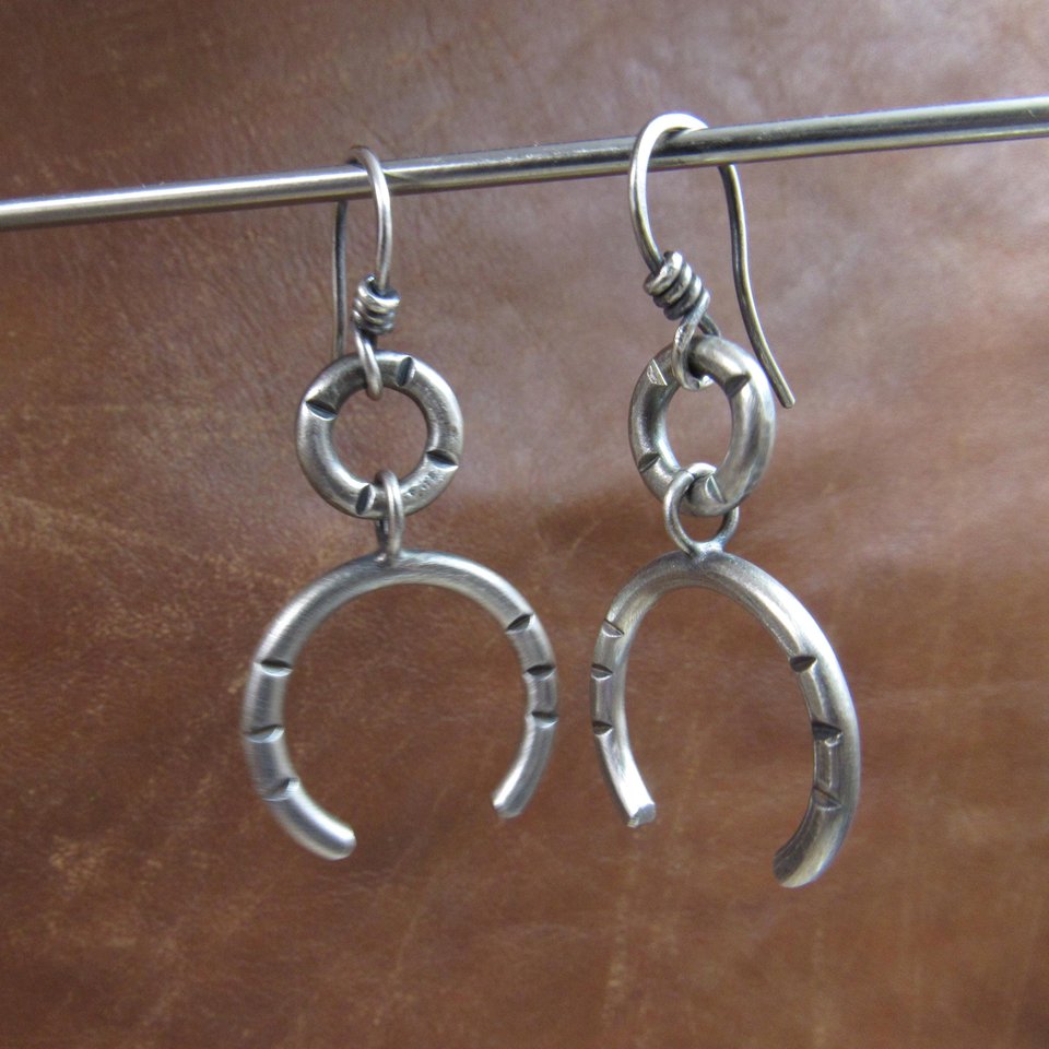 Bold and simple contemporary argentium sterling silver earrings shown hanging  have lovely swingy movement. The double open hoop design allows for them to articulate. Lightweight and comfortable  at only 5 grams per earring. 1.75” long and 7/8” at widest point. Displayed dangling on stand against brown leather.