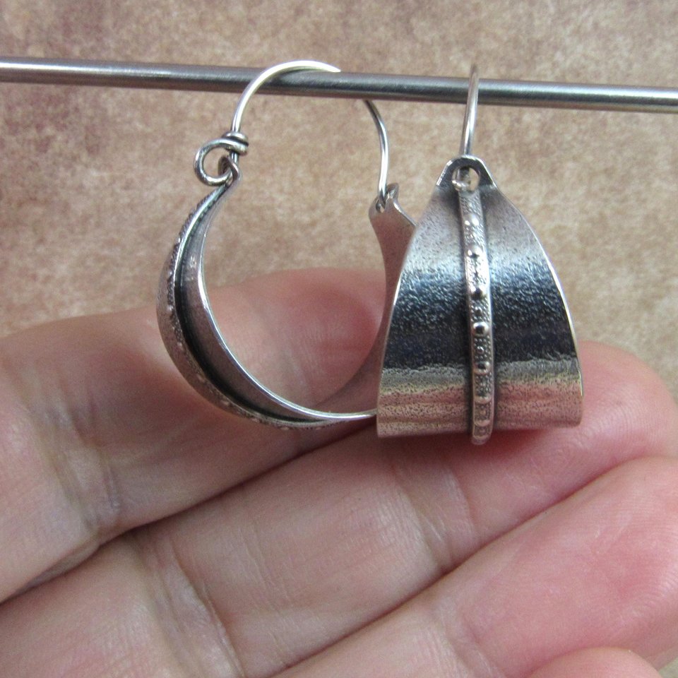 Sterling silver hoop earrings basket style fancied up with a strip of patterned  silver wire against textured argentium silver. A perfect sterling silver hoop earring for every occasion!  Oxidized, polished, finished with sterling ear wires. 1.25" or 3.1cm tall,  7/8" or 2.22cm wide. Displayed against fingers  on neutral background.