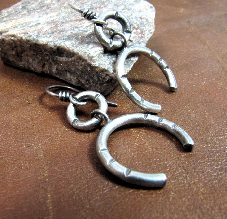 Side view of contemporary sterling silver earrings crafted from Argentium have lovely swingy movement. The double open hoop design allows for them to articulate. Lightweight and comfortable  at only 5 grams per earring. 1.75” long and 7/8” at widest point. Displayed on brown leather and rock.
