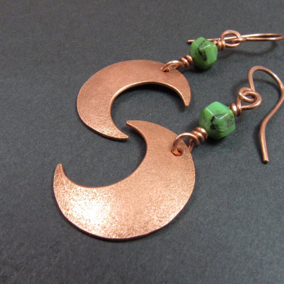 Handmade copper crescent moon dangle earrings with faceted green chrysoprase beads. Earrings measure 2 and 1/8" long and the moon is 3/8" wide at widest point.The ear wires are solid, pure copper. Displayed on dark background.