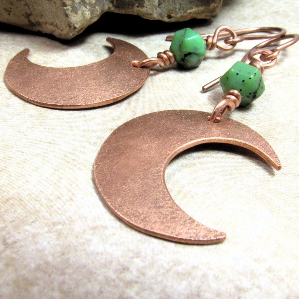 Up close pic of handmade copper crescent moon dangle earrings with faceted green chrysoprase beads. Earrings measure 2 and 1/8" long and the moon is 3/8" wide at widest point.The ear wires are solid, pure copper. Displayed on neutral background with rock.