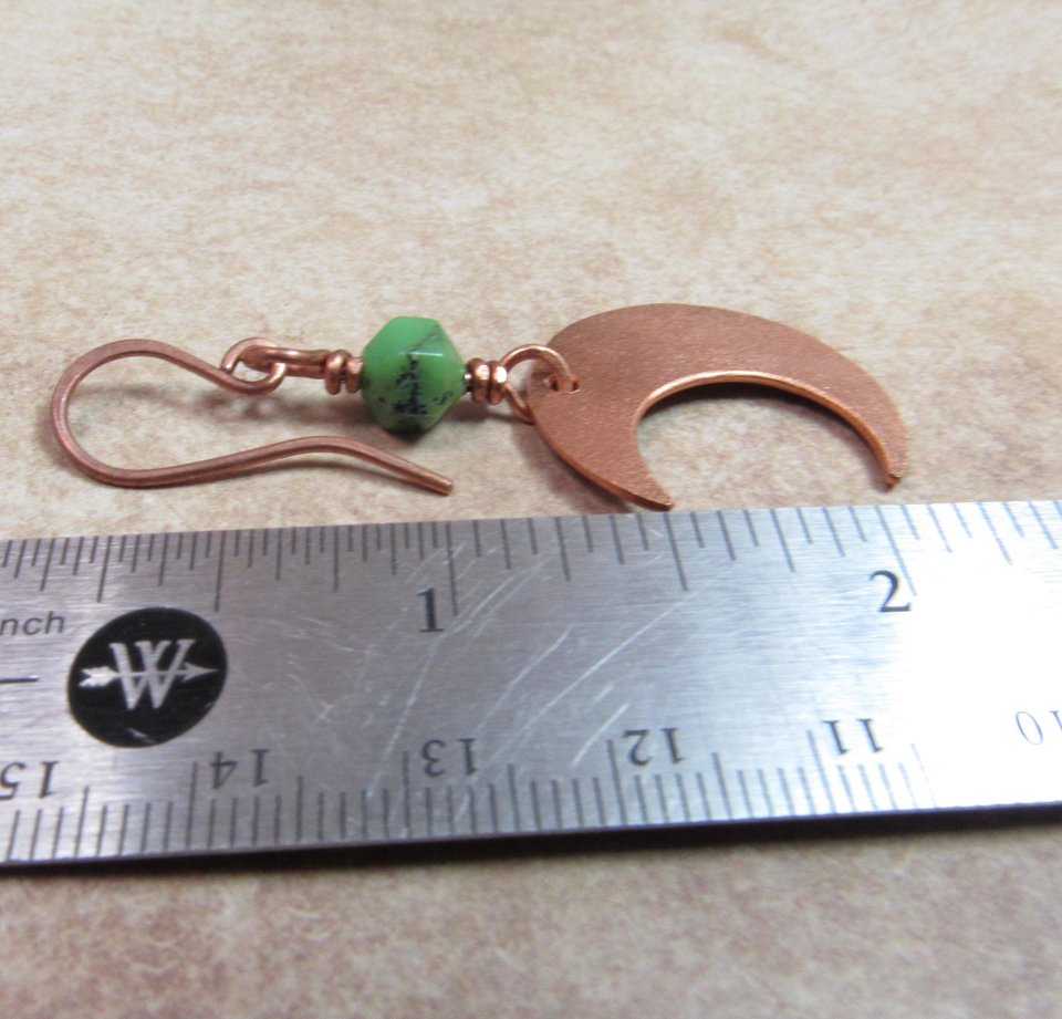 Handmade copper crescent moon dangle earrings with faceted green chrysoprase beads. Earrings measure 2 and 1/8" long and the moon is 3/8" wide at widest point.The ear wires are solid, pure copper. Displayed against ruler on neutral background.