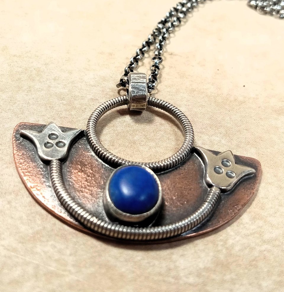 Handcrafted mixed metal lotus pendant in argentium silver and copper with lapis lazuli cabochon. Displayed on neutral background.