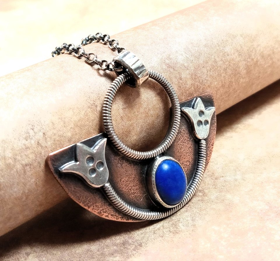 Side view of handcrafted mixed metal lotus pendant in argentium silver and copper with lapis lazuli cabochon. Displayed on neutral background.