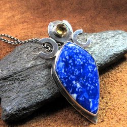 Triple goddess / moon pendant necklace with a faceted citrine and large lapis lazuli cabochon crafted from argentium sterling silver, fine silver. Pendant measures 2 inches from the top and is 7/8 inch across widest part and is suspended on a 18 inch sterling silver chain. Displayed against dark rock on brown leather.